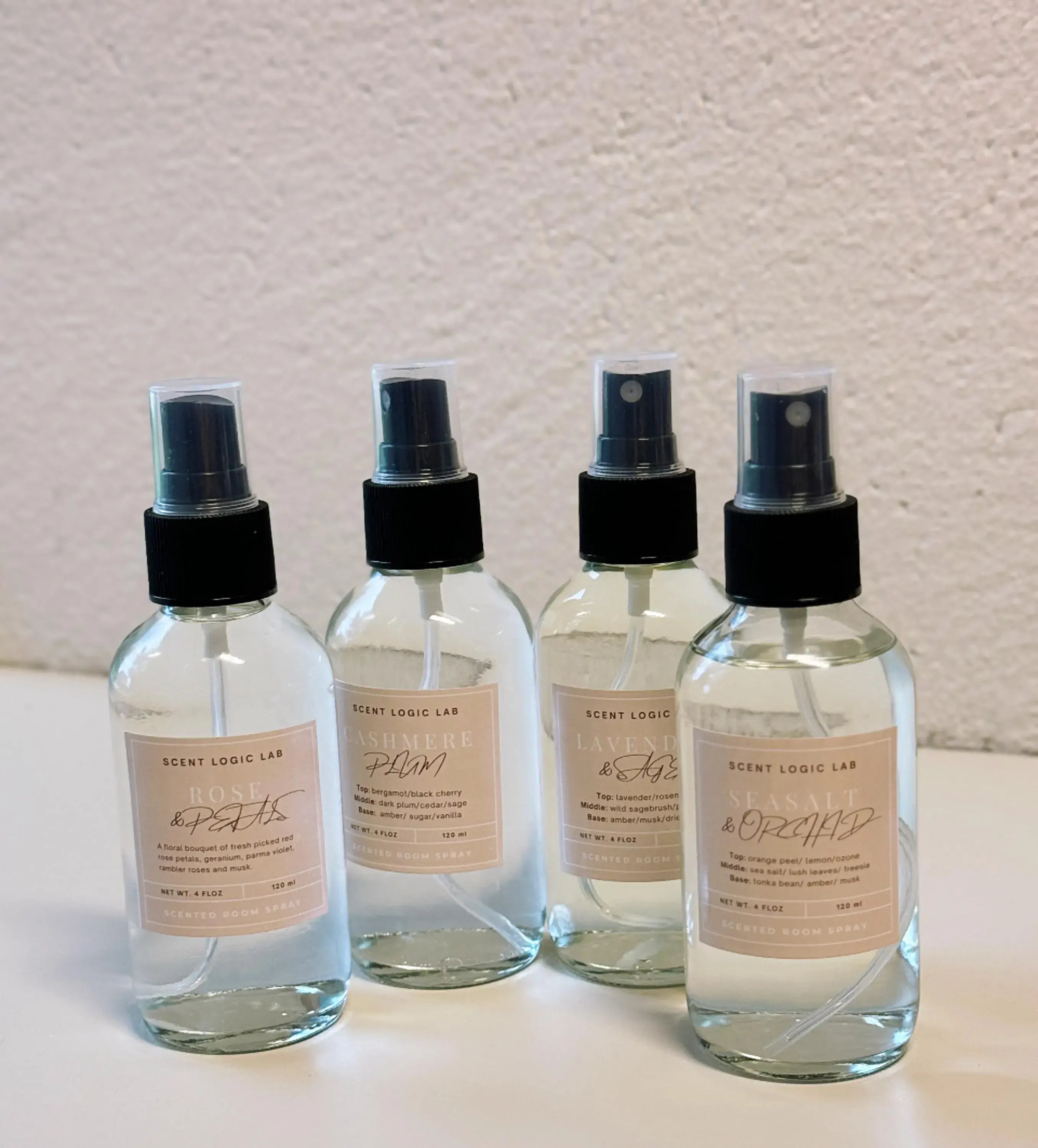 Four spray bottles with labels on a light surface and textured wall background