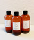 Three amber-colored bottles with black caps on a textured beige background
